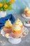 Cute Easter chick cupcakes. Vanilla cupcakes with buttercream on a white stand with fresh flowers on a white wooden background.