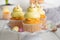 Cute Easter chick cupcakes. Vanilla cupcakes with buttercream on a white stand with fresh flowers on a white wooden background.