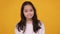 Cute eastern girl shrugging shoulders and spreading hands, feeling unsure and doubtful, orange studio background