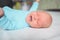 Cute emotional crying newborn infant boy in blue jumpsuit laying on bed. Baby facial expressions.