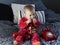 Cute fair baby girl sitting on bed sucking on vintage red telephone cord