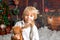 Cute fashion toddler boy, playing in the snow with teddy bear in front of a wooden cabin log