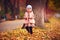 Cute fashionable baby girl walking in autumn park among fallen leaves
