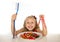 Cute female child eating dish full of sweets and holding huge toothbrush in dental care and health concept