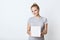 Cute female teenager with hair knot, wearing t-shirt, holding white box in hands, preparing surprise for her mother. Adorable fema