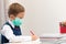 A cute first grader boy in a school uniform at his desk wearing a protective medical mask during the coronavirus pandemic