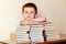 A cute first-grader is sitting at the table, putting his hands on books