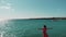 Cute fit woman in red dress with hands apart standing on the cliff. Lady in red on rocky beach with arms apart in air. Aerial shot