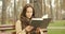 Cute focused woman turns pages of a book and reading while sitting on bench in autumn cold park wearing brown scarf alone.