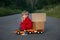 Cute four-year-old boy in a red overalls sits on a large toy car - a truck with cardboard boxes - parcels