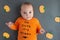 Cute funny baby wearing halloween orange long sleeve shirt with bat silhouette and pumpkin toys laying on the background