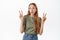 Cute and funny blond girl shows peace v-sign and pucker lips silly, standing happy in summer t-shirt and jeans against