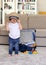 Cute funny happy little baby boy staying at home putting straw hat on head with blue suitcase at background packed for vacation