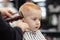 Cute ginger baby boy with blue eyes in a barber shop having haircut by hairdresser. Hands of stylist with tools.