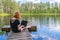 Cute ginger girl sitting on wooden planked footway and working with laptop in summer day against beautiful landscape of northern