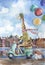 Cute giraffe driving retro scooter holding colorful balloons in one hand on european city landscape background