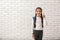 Cute girl with backpack and raised finger on white brick background