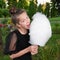 Cute girl bites delicious cotton candy and has fun in the park. Happy teen girl and sweet treat