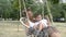 Cute girl with a child swinging on a swing that hang on a tree in the park. A little boy sits on his mother`s lap, they