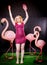 Cute girl in fuchsia sequins dress resting and dancing with three big flamingos on black background