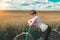Cute girl with ginger hair standing near the old bicycle. Pretty woman and vintage bike among of golden wheat fields at sunny summ