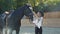Cute girl in hat caresses black mare`s head on sunny background