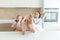 Cute girl and her mother are smiling while eating ice cream in the kitchen with legs on a table