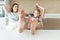 Cute girl and her mother are smiling while eating ice cream in the kitchen with legs on a table