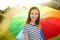 Cute girl holding colorful rainbow umbrella on rainy summer day. Child walking under warm rain outdoors. Outdoor summer activities