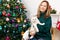 Cute girl holding a funny, disgruntled white cat against the background of a Christmas tree. Looking at the camera