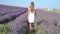 Cute girl in lavender flowers field at sunset in purple dress