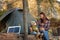 Cute girl looks at child sitting on log in forest near solar panel and tent camp