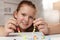 Cute girl making beaded jewelry at table in room