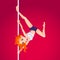 Cute girl performing pole dance. Young, slim and beautiful redhead woman takes on a pylon. Pole acrobatics. Bright red background