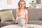 Cute girl putting coin into piggy bank at table in living room