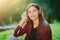 Cute girl`s face with headphones. Young woman enjoys music while sitting in green park. Concept of youth, freedom