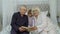 Cute girl with senior retired grandmother and grandfather sitting on bed reading book in bedroom