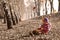 Cute girl sitting on fallen autumn leaves while leafs falling and playing with dolls