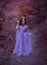 Cute girl is standing in the forest in a purple light long dress with flowers, a little princess like in a dream, walks