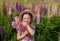 Cute girl in a straw hat and a purple plaid shirt holds a large bouquet of wild flowers. lupine field