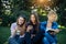 Cute girl students spend free time sitting on green grass in the park on summer day. One woman is reading a book and two young