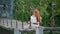 Cute girl with thick beautiful fiery red hair sits on suspension bridge over river and reads book