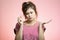 Cute girl is upset by the result of a pregnancy test on a pink studio background, concept of family planning and motherhood