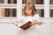 Cute girl in white reading book in library