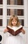 Cute girl in white reading book in library