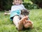 Cute gray-brown tabby kitten sits on the small bare feet of a child on the lawn on a warm sunny summer day