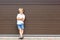 Cute grumpy blond child in casual clothing standing against brown garage door. Angry kid boy with crossed arms near house.Awkward