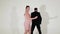 Cute guy in black suit with shirt and pregnant woman are dancing in light room.