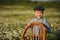 Cute handsome boy wearing jeans and shirt sitting on wooden chair on meadow of chamomiles daisy and smiling enjoying summer day in