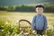 Cute handsome boy wearing jeans and shirt sitting on wooden chair on meadow of chamomiles daisy and smiling enjoying summer day in